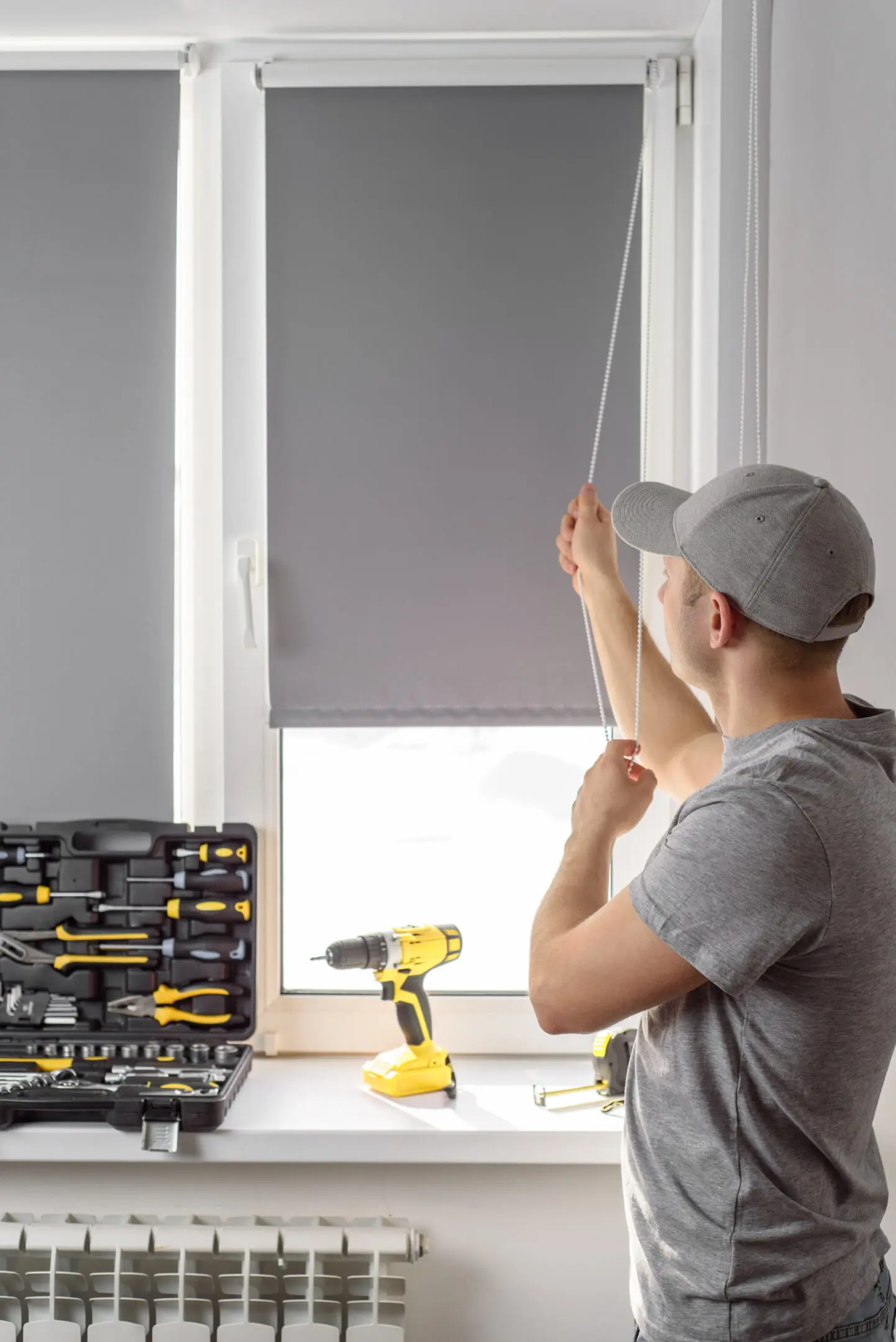 Man installing a gray roller blind on a window.